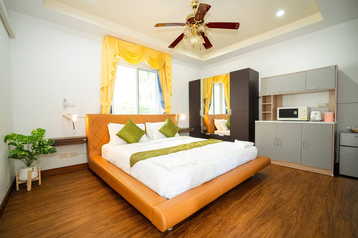 Un dormitorio moderno con una cama grande, suelo de madera, ventilador de techo y armario empotrado.