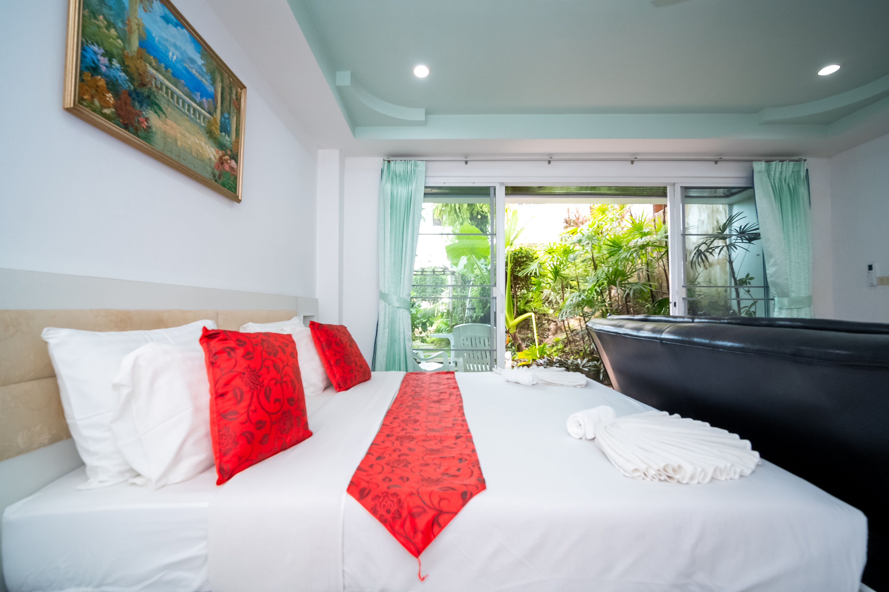 Quarto de hotel com cama, uma janela grande com cortinas, um quadro na parede e vista para área verde lá fora.