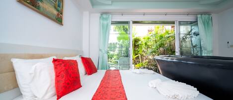 Quarto de hotel com cama, uma janela grande com cortinas, um quadro na parede e vista para área verde lá fora.