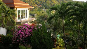 Una casa con balcón que da a un jardín exuberante y una colina boscosa.