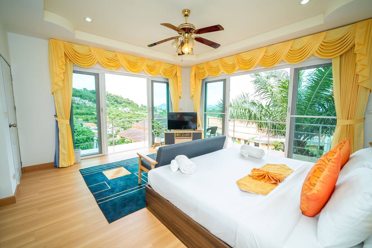 Habitación de hotel con cama, televisor, escritorio y balcón con vistas a zonas verdes.