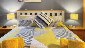 A neatly made bed with patterned bedding, two bedside lamps, and a wall-mounted artwork of orchids. - 2 bedroom accommodation in Filey (Filey)