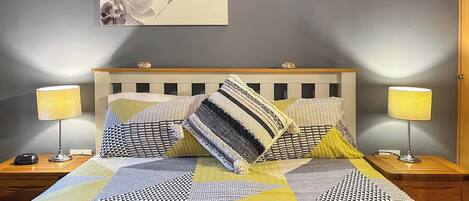 A neatly made bed with patterned bedding, two bedside lamps, and a wall-mounted artwork of orchids.