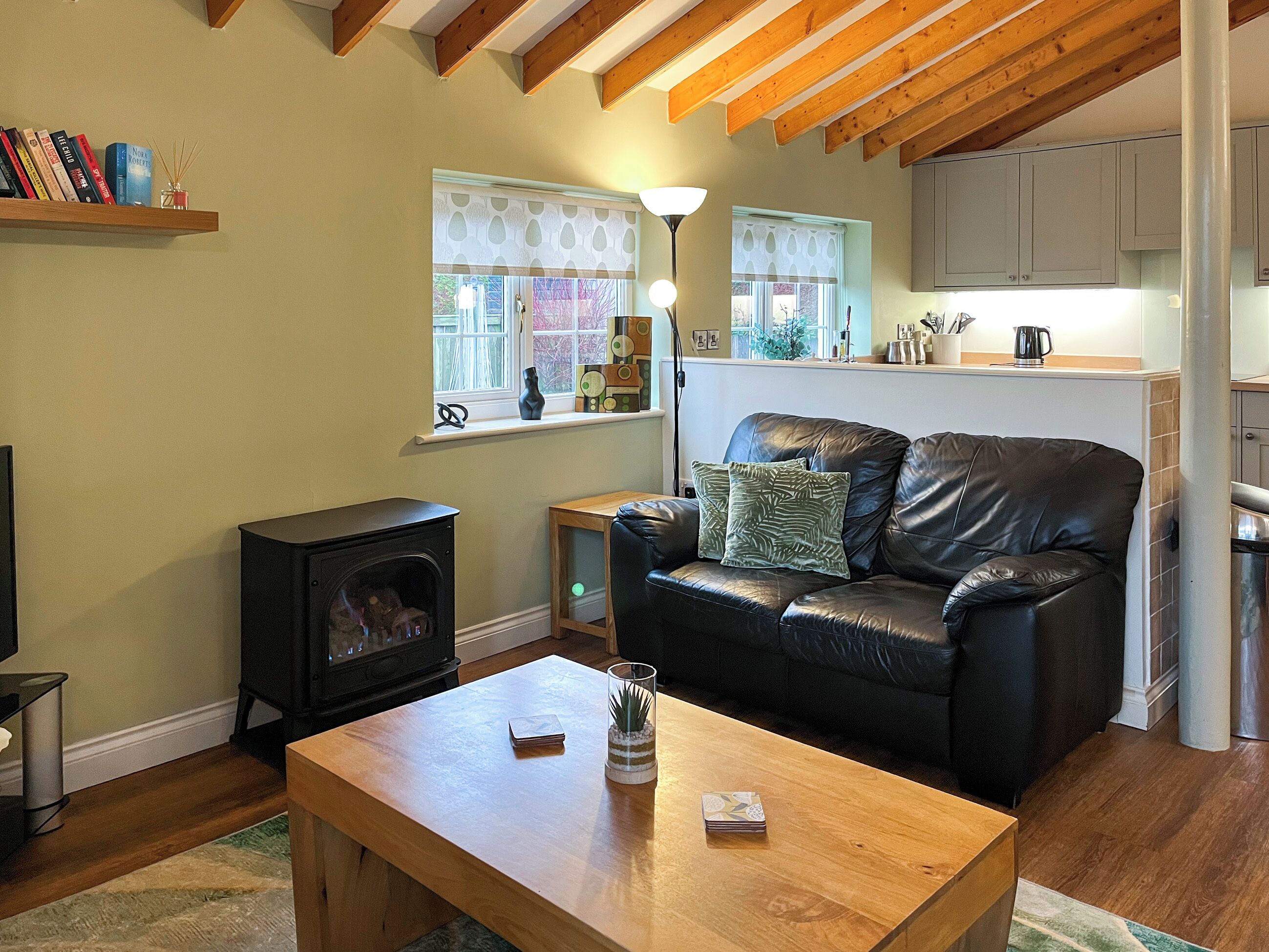 A cozy living room with a fireplace, a leather sofa, a wooden coffee table, and a kitchen in the background.