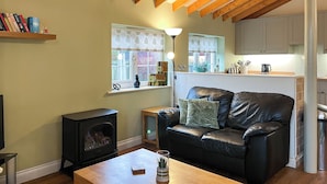 A cozy living room with a fireplace, a leather sofa, a wooden coffee table, and a kitchen in the background. - 2 bedroom accommodation in Filey (Filey)