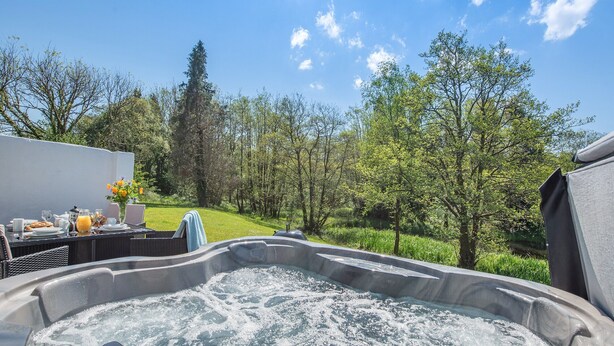 Una vasca idromassaggio immersa in un rigoglioso giardino, con cielo sereno.