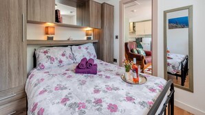 Una camera da letto con un letto, un comodino, uno specchio e vista sulla cucina.