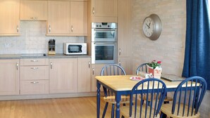 Une cuisine moderne avec des meubles en bois, un four à micro-ondes, un four traditionnel et un coin repas avec des chaises bleues et une table en bois.