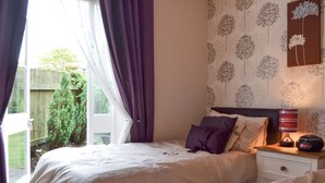 A bedroom with two beds, a nightstand with a lamp, and a wall with floral wallpaper. - 3 bedroom accommodation in York (York)