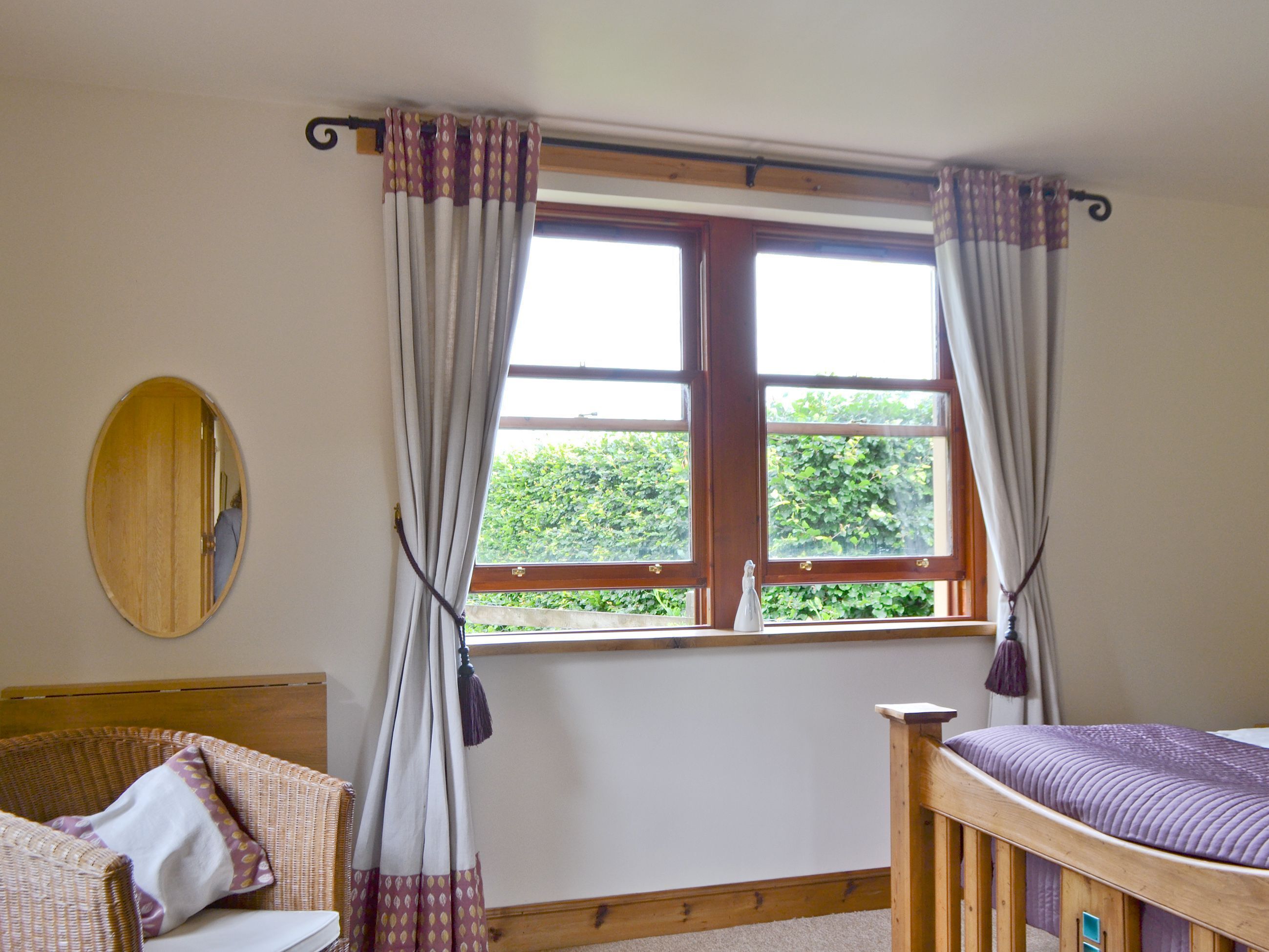 A room with a wooden bed, a wicker chair, a mirror, and a window with curtains.