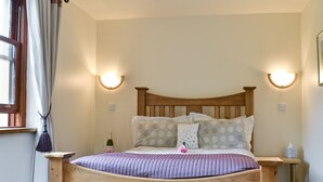 Un dormitorio con cama de madera, dos mesitas de noche, un tocador, una ventana con cortinas e iluminación en la pared.