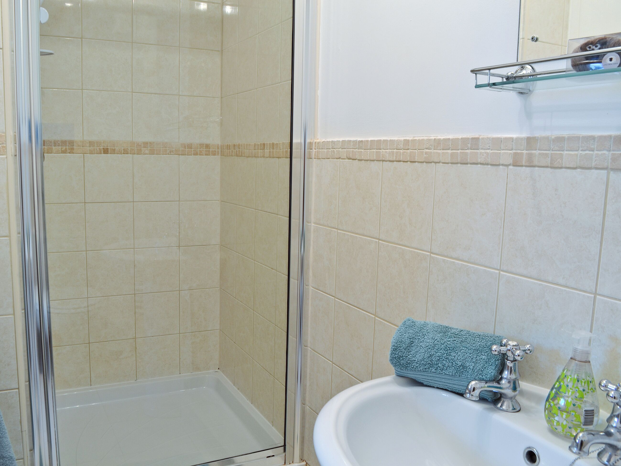 A bathroom with a glass shower enclosure, a sink with a mirror above it, and a towel on the sink.