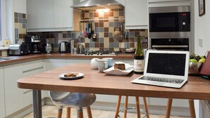 A modern kitchen with a wooden table, a laptop, and a bottle of wine.