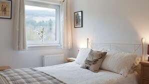 A bedroom with a bed, a window with curtains, a radiator, a bedside table, and a wall-mounted picture.