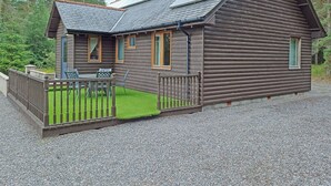 A log cabin with a gravel driveway, a fenced patio, and a small deck. - 3 bedroom accommodation in Strachan, near Banchory (Strachan, near Banchory)