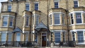 A multi-story building with a brick facade, bay windows, and a sign indicating it is a holiday accommodation. - 2 bedroom accommodation in Filey (Filey)