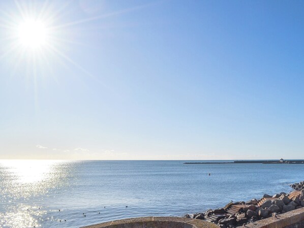 A coastal scene with a clear sky, calm sea, and a rocky breakwater.