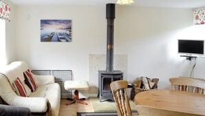 A cozy living room with a sofa, a coffee table, a dining table, and a fireplace. - 2 bedroom accommodation in Wootton Fitzpaine, near Charmouth (Wootton Fitzpaine, near Charmouth)