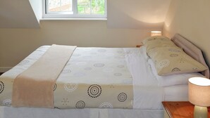 A bedroom with a bed, pillows, a bedside lamp, and a window with a view of greenery. - 2 bedroom accommodation in Wootton Fitzpaine, near Charmouth (Wootton Fitzpaine, near Charmouth)