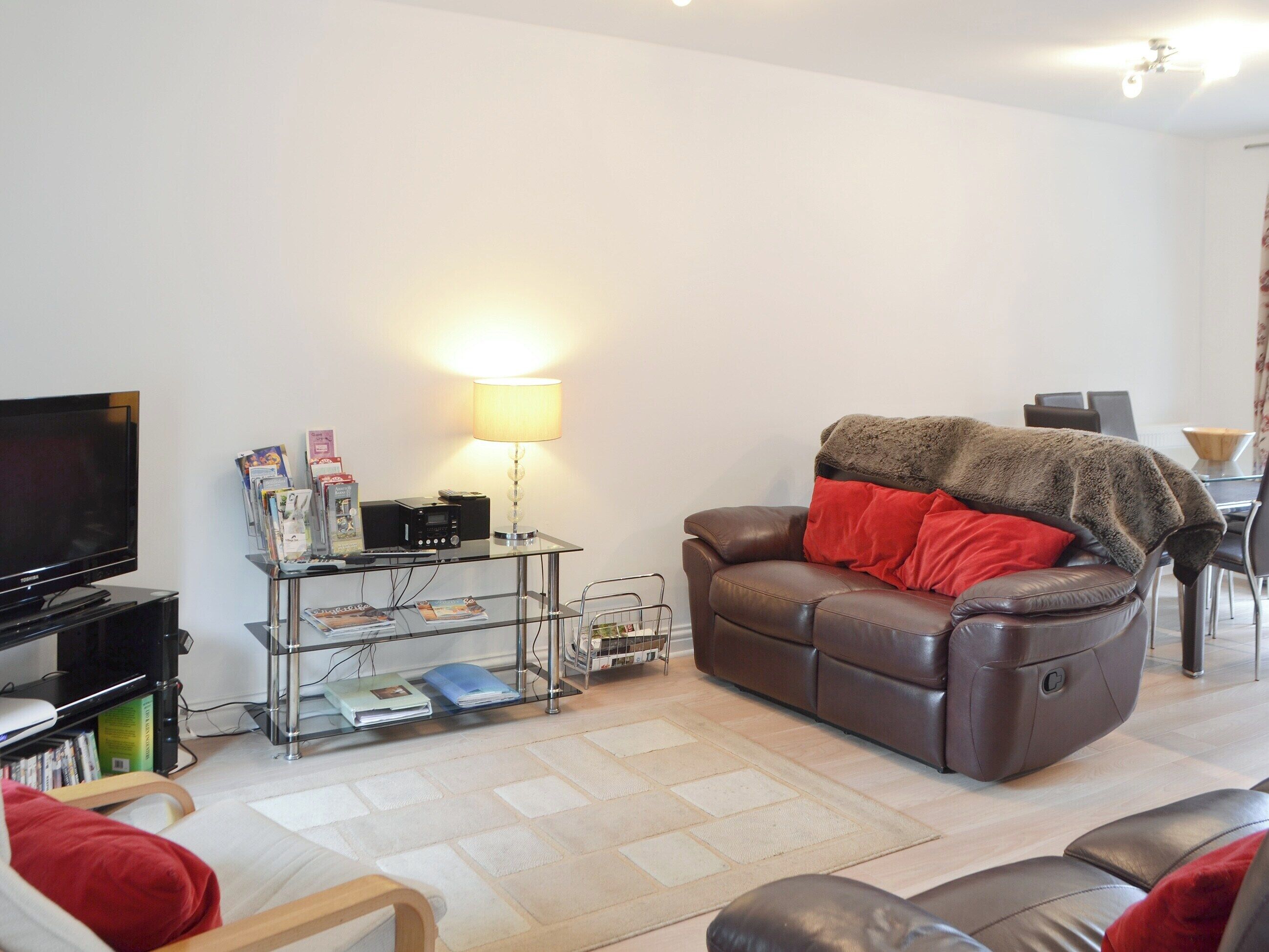 A living room with a leather sofa, a flat-screen TV, a glass coffee table, and a lamp.