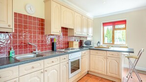 A kitchen with beige cabinets, a red-tiled backsplash, a microwave, and a window with a red curtain. - 1 bedroom accommodation in St Osyth (St Osyth)