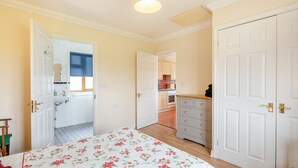 A bedroom with a floral bedspread, a wardrobe, and a view into the kitchen. - 1 bedroom accommodation in St Osyth (St Osyth)
