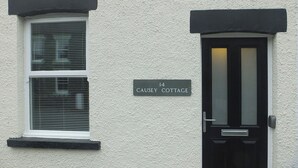 Et hvidt hus med en sort dør og vindueskasser. Et skilt på væggen viser "14 Causey Cottage".