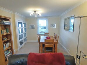 A dining area with a table and chairs, a bookshelf, a ceiling fan, and a window with blinds.