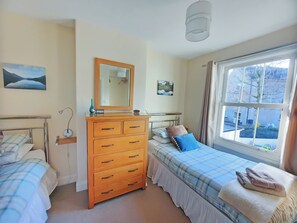 A bedroom with two beds, a dresser, a mirror, and a window with a view.