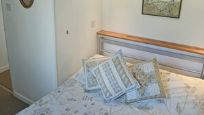 Une chambre à coucher comprenant un lit, une tête de lit, un miroir fixé au mur et une carte encadrée.