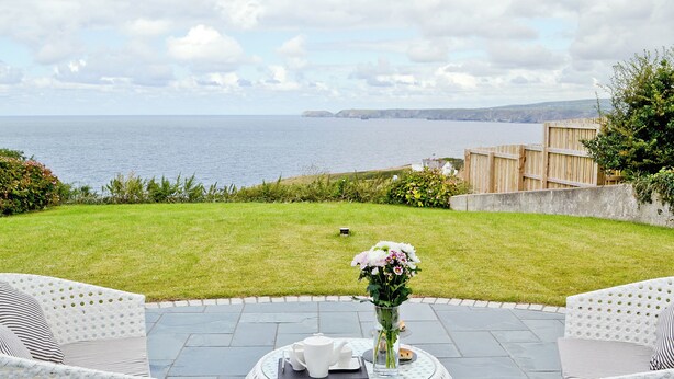 A patio with white wicker furniture, a round table with a vase of flowers, and a view of the sea. - 1 bedroom accommodation in Port Isaac (Port Isaac)