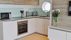 A modern kitchen with white cabinetry, a built-in oven, a microwave, a kettle, and a sink. - 1 bedroom accommodation in Port Isaac (Port Isaac)