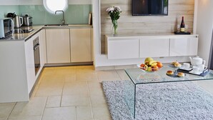 A modern kitchen with a built-in oven, a round window, and a flat-screen TV mounted on a wooden wall. - 1 bedroom accommodation in Port Isaac (Port Isaac)