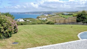 A coastal landscape with grassy areas, a wooden fence, and buildings in the distance. - 1 bedroom accommodation in Port Isaac (Port Isaac)