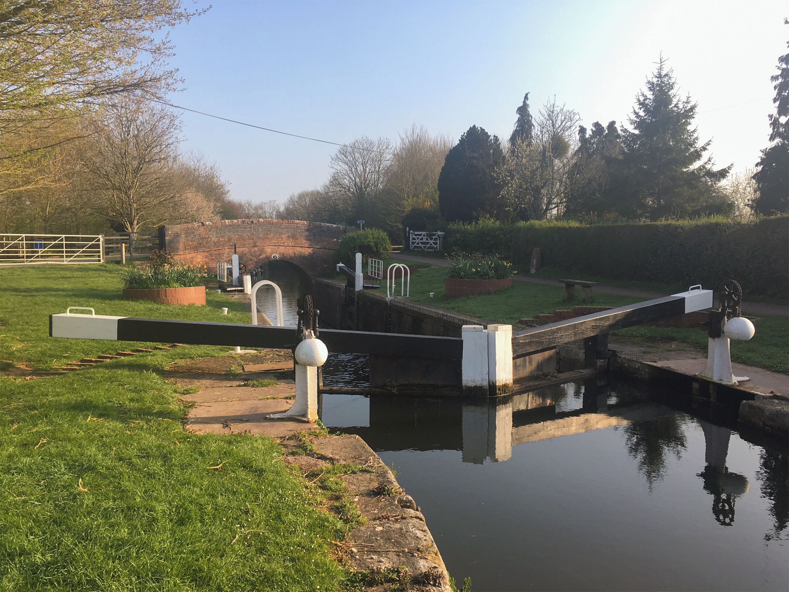 Une écluse sur un canal, avec un pont, des berges verdoyantes et des arbres en arrière-plan.