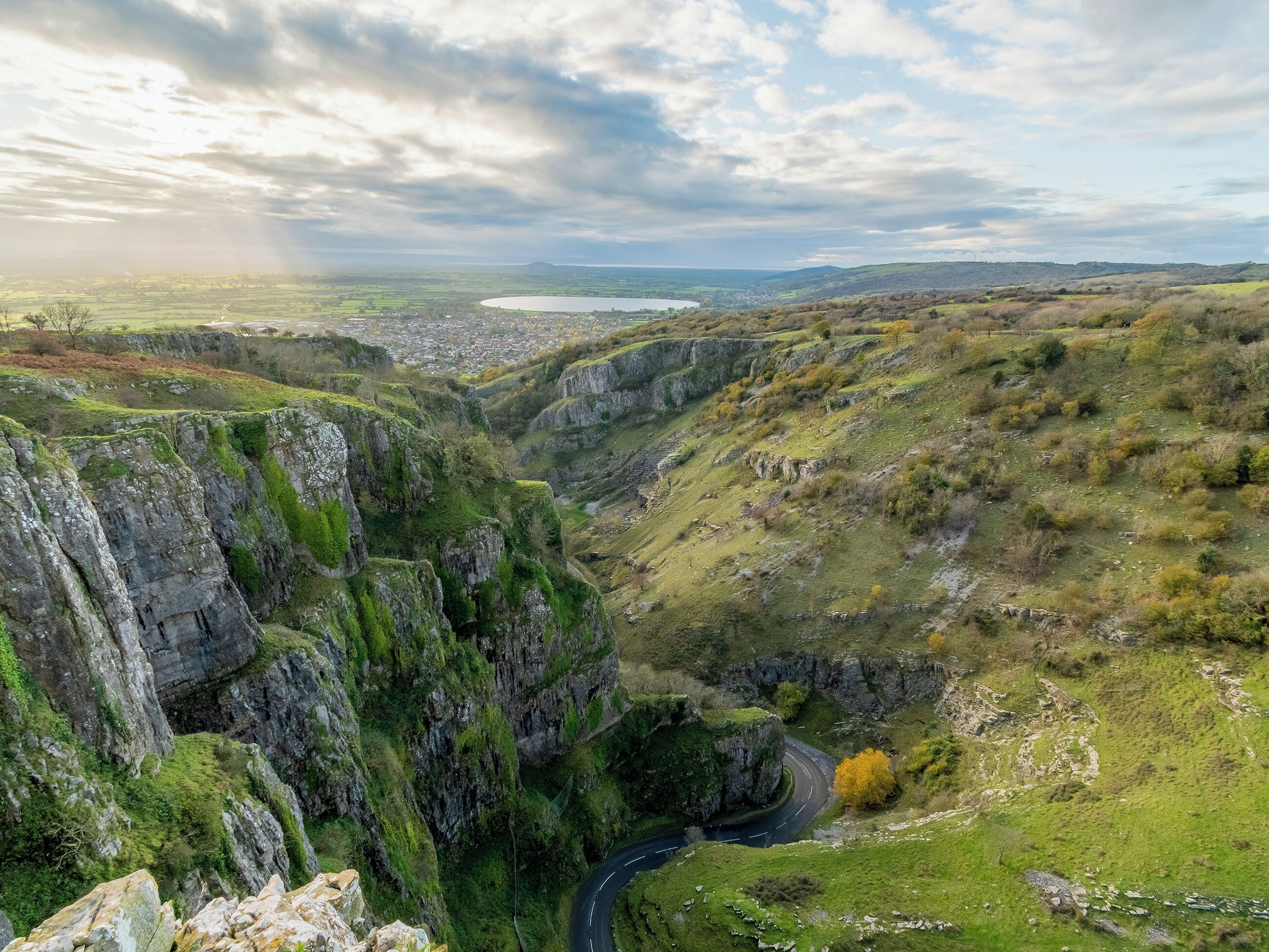 A valley with a winding road, rocky cliffs, and a distant town.