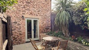 A stone building with a patio featuring a round table and wooden chairs.