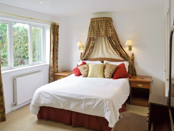 A bedroom with a large bed, a window with curtains, a radiator, and two bedside lamps.