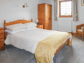 Un dormitorio con una cama de madera, una mesita de noche, un armario, una silla y una ventana con cortinas.