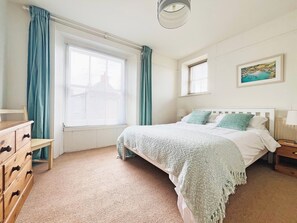 A bedroom with a bed, a dresser, a window with curtains, a painting on the wall, and a lamp on the nightstand. - 4 bedroom accommodation in Port Isaac (Port Isaac)