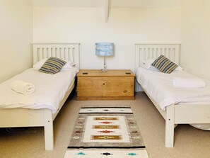 Une chambre double avec deux lits simples, une table de chevet en bois avec une lampe et un tapis à motifs.