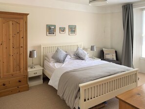 A bedroom with a wooden wardrobe, a bed with white bedding, a nightstand with a lamp, and a window with grey curtains. - 4 bedroom accommodation in Port Isaac (Port Isaac)