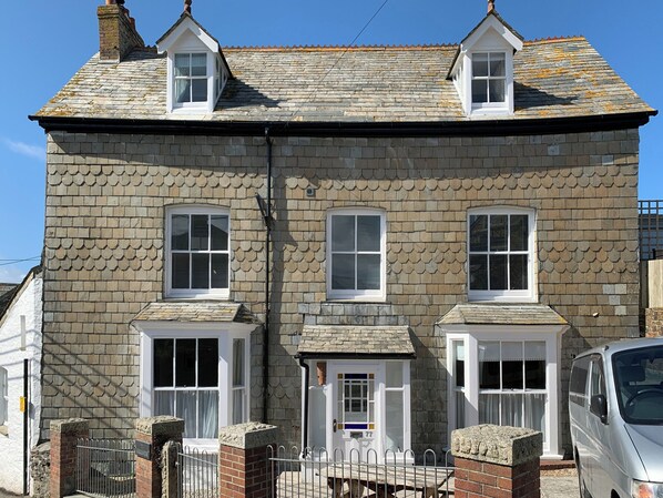 A two-story stone house with a gabled roof, multiple windows, and a small porch area.