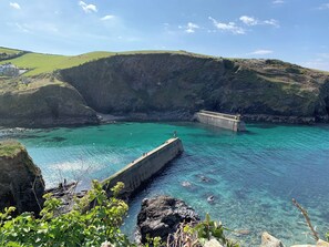 A coastal landscape with a clear blue sea, a concrete pier, and rocky cliffs.