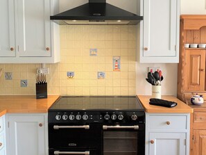 A kitchen with a black stove, white cabinets, and a tiled backsplash featuring nautical tiles. - 4 bedroom accommodation in Port Isaac (Port Isaac)