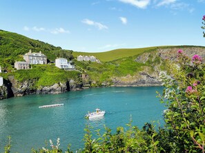 A coastal scene with houses on a hillside, a boat on the water, and lush greenery.