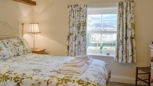 Ein Schlafzimmer mit einem großen Bett, einer Nachttischlampe, einem Fenster mit blumigen Vorhängen und Blick ins Freie.