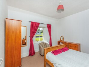 A bedroom with a wooden bed, a wooden dresser, a mirror, a window with curtains, and a radiator. - 2 bedroom accommodation in Fort Augustus (Fort Augustus)