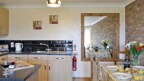 A modern kitchen with a central island, a dining area with a table set for breakfast, and a brick wall in the background.
