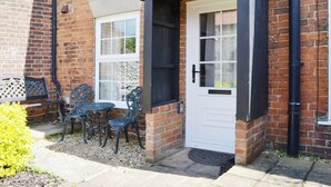 A brick house with a white door and a small porch. There are two outdoor tables and chairs. - 2 bedroom accommodation in Docking (Docking)